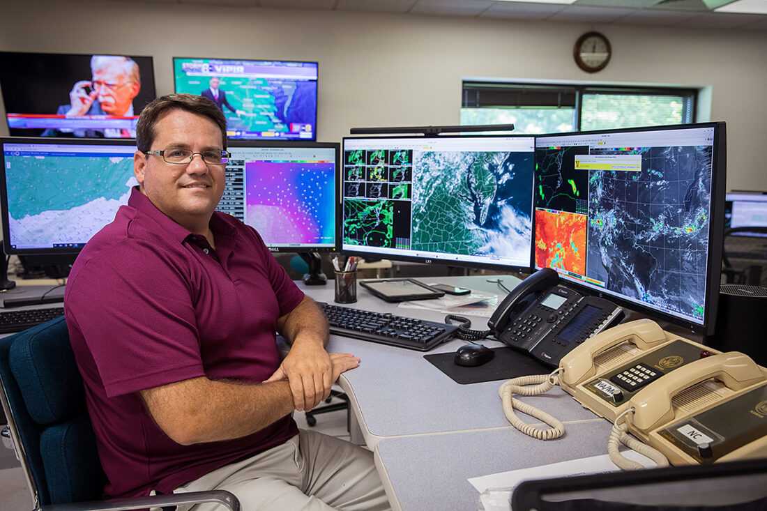 NOAA کے موسمیاتی ماہر کی اس کے NOAA موسمی خدمت کے دفتر کے ورک سٹیشن کے سامنے ایک تصویر